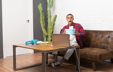 African american man with laptop in the living room holding gift boxes in hands