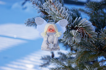 Christmas angel on a snowy branch of a Christmas tree. Handmade holiday decorations. Natural photo...