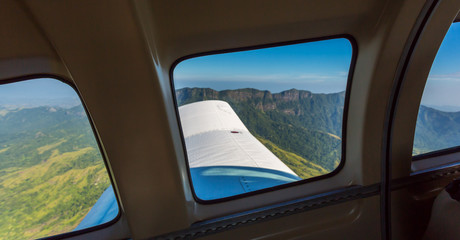Stunning view of mountain range from a window of a small airplane during take off. Air travel in Fiji, Melanesia, Oceania. Green lush vegetation on emerald mountains and valleys of Viti Levu island