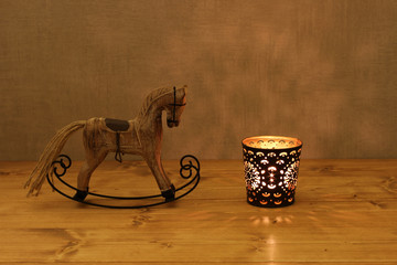 Fototapeta na wymiar Christmas decoration - wooden toy rocking-horse and candle in candlestick on the table against concrete wall
