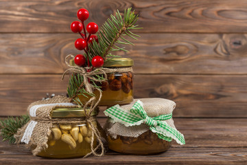 Honey jars with nuts in gift packaging kraft. Wreath. Christmas winter frame on dark wooden background. Red elements