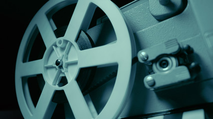 Obraz premium Film projector with dramatic blue lighting and selective focus. Retro film production still life. Concept of film-making. Old 8mm projector is turning off. Close-up of a reel with a film