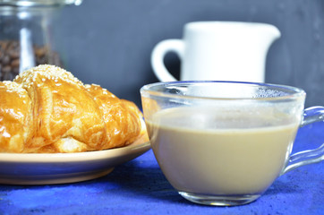 A plate with croissant cup of black with milk coffee and. Top View. The croissant is decorated with sesame. Complement the composition of a coffee beans and milk jug. healthy breakfast. good morning.