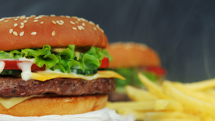 Big appetizing burger with meat cutlet, vegetables, cheese, lettuce and sauce. Hamburger rotates on other meal background, close-up view. Unhealthy yummy food concept
