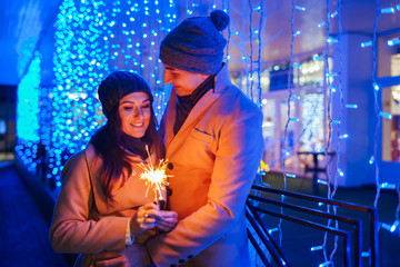 Young loving couple burning sparklers by holiday illumination