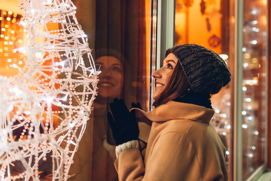 Young woman walking in city and looking at decorated Christmas showcases at night.