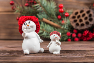 Two snowman figurines in red hats, white snowflakes on a dark wooden textured background. Christmas toys