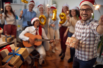 Smiling business man have fun in Santa hat at Xmas party with his colleagues.