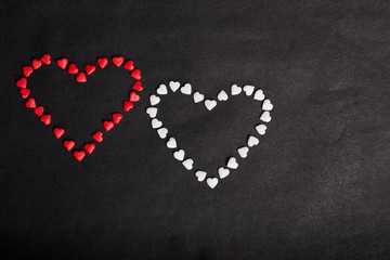 Two heart-shaped red and white candies on black backdrop.