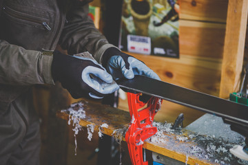 A male worker in a ski service workshop repairs the sliding surface of the skis. Close-up of a hand...