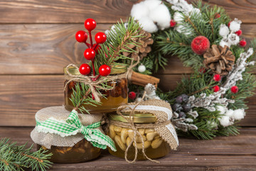 Honey jars with nuts in gift packaging kraft. Wreath. Christmas winter frame on dark wooden background. Red elements
