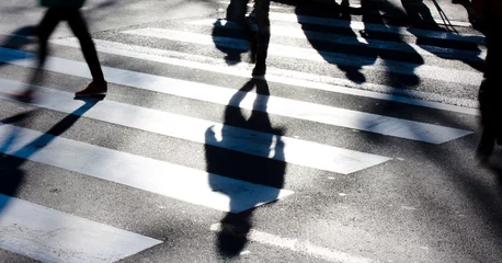 Poster Blurry zebra crossing with pedestrians making long shadows © Aleksandra