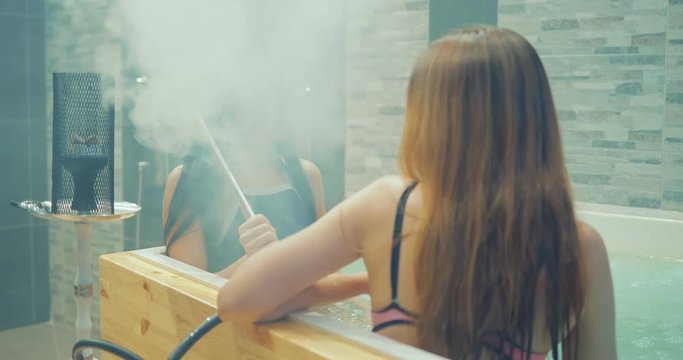 Sexy girls smoke hookah in the pool. Girls are blowing smoke. Portrait view.