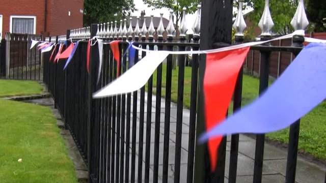 Red, white and blue British colours festive bunting on metal fence in residential area in England, United Kingdom on a rainy day