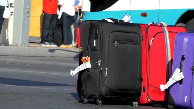 Airport to holiday resort transfer. Man loading stack of baggage onto the bus outdoors, people in the background