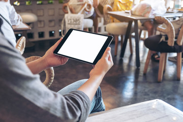 Mockup image of a woman holding black tablet pc with blank white screen while sitting in cafe