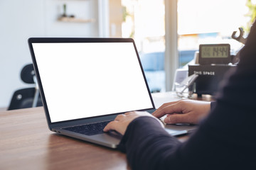 Mockup image of a woman using and typing on laptop with blank white desktop screen on wooden table in office
