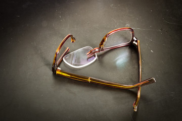Broken eyeglasses on desk; lens of glasses fell out of broken frames.