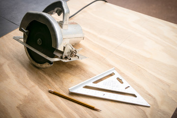 Circular saw, pencil, and speed square - tools on a plywood board ready for a construction project.