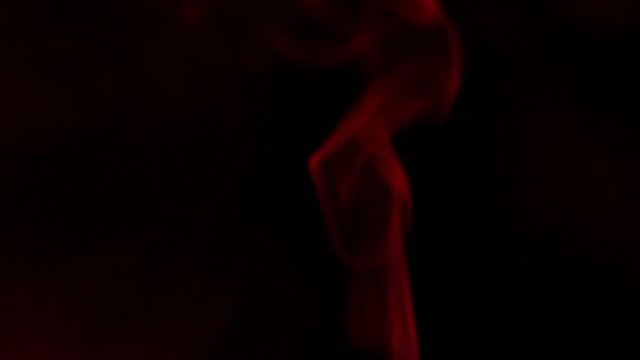 Red smoke cloud bursts and wisp drifts in the dark; burning incense or an evil spirit.