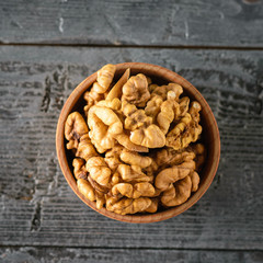 Clay bowl with the kernels of walnuts on the black wooden table. The view from the top.