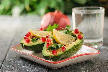 A glass of clean water with avocado halves filled with pomegranate seeds and herbs. Vegetarian cuisine for weight loss.