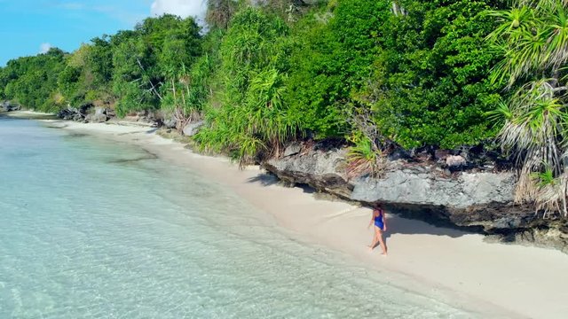 Aerial: woman walking on tropical beach, scenic turquoise water and white sand, Tomia Island, Wakatobi marine national park, Indonesia, paradise travel destination