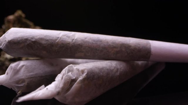 Up close panning view of marijuana rolled in joint sitting on black surface.