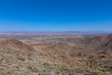 A desert panorama with rock formations and distant mountain chain on horizon. A view from Joshua Tree National Park trail onto valleys and mountains, California USA.