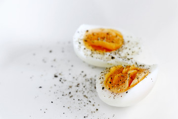 Hard boiled eggs sprinkled with black pepper on a white background with copy space