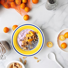 Healthy breakfast smoothie bowl topped with kumquat, coconut chips and chia seeds on a marble background with copy space