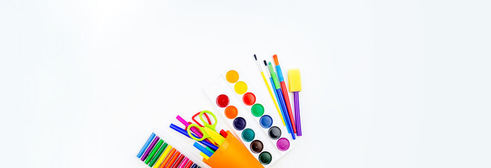 Pencils and felt-tip pens in a plastic cup, paints and pastel crayons on a white background