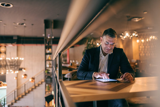 Smiling middle-aged man dressed smart casual sitting in cafe and using tablet.