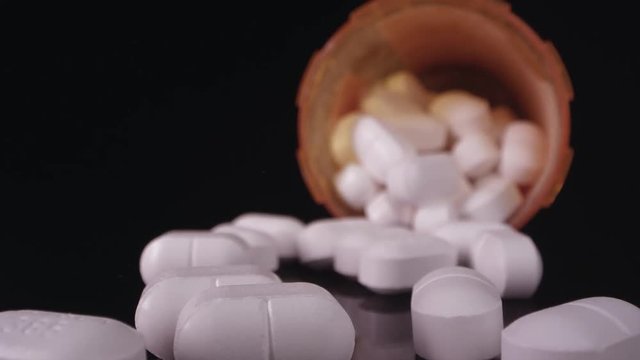 Prescription drugs being poured out onto black table top as they scatter.