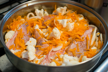 Mediterranean sea bass with cauliflower and carrots in a pan. Cooking process.