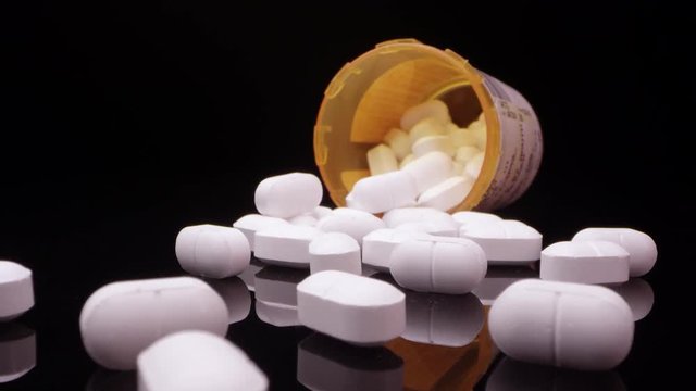Moving over top of prescription opioid drugs on black table moving in towards bottle on its side.