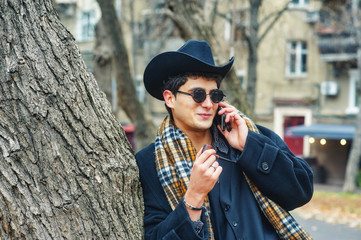 a man smokes a pipe in the city . portrait of a stylish fashionable man on the streets . man in black coat, plaid scarf and hat