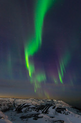 Beautiful northern lights, aurora in the night sky over the snow-covered hills.