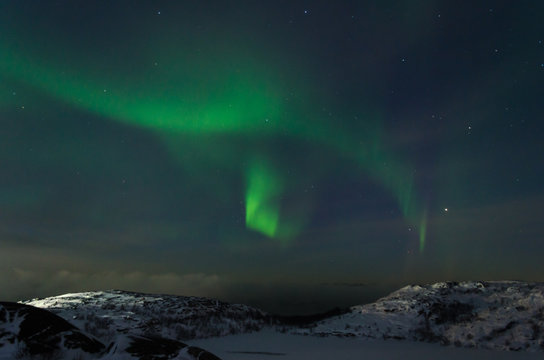 Beautiful northern lights, aurora in the night sky over the snow-covered hills.