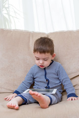 toddler boy is using a tablet on a couch