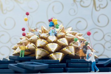 Miniature group happy family holding balloons standing on gold gift bow.