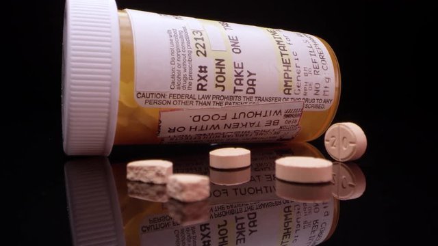 Moving in towards prescription amphetamine pills on table top next to bottle.