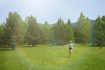 Teen girl in shorts and a blue T-shirt on a clearing with green grass and trees.
