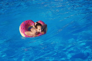 Girl teenager in a swimsuit swims with an inflatable ring in the pool with blue water.