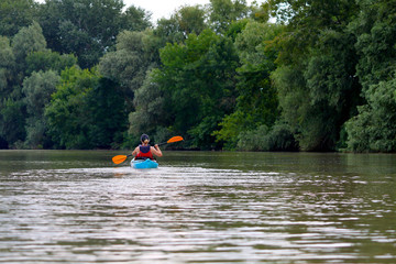 Kayaking. A Woman in blue kayak. Girl paddling in the calm summer Danube river near the shore with green trees