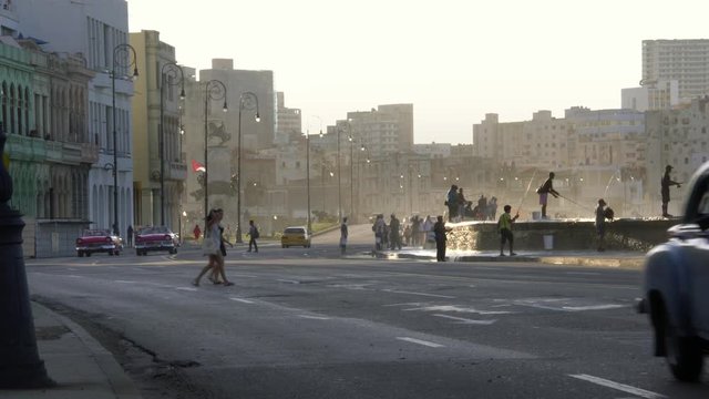 old 1950's Vintage classic american cars driving on famous waterfront malecon promenade, waves splash on fishermen, Old Havana, Cuba