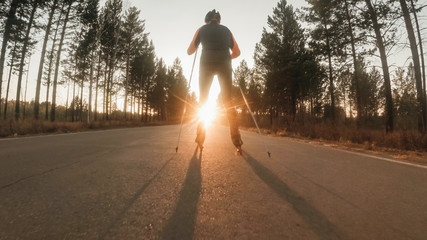 Training an athlete on the roller skaters. Biathlon ride on the roller skis with ski poles, in the helmet. Autumn workout. Roller sport. Adult man riding on skates. © ivandanru
