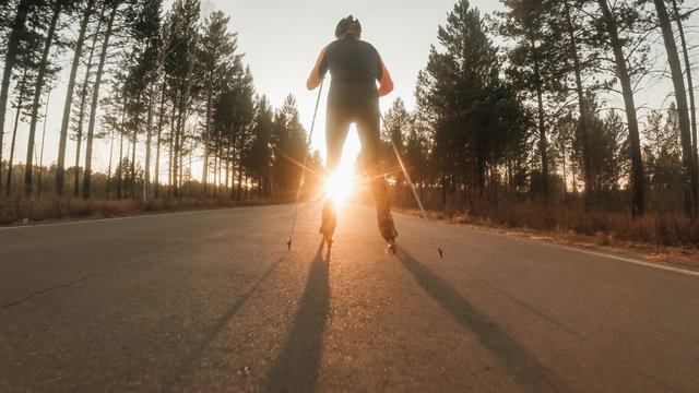 Training an athlete on the roller skaters. Biathlon ride on the roller skis with ski poles, in the helmet. Autumn workout. Roller sport. Adult man riding on skates.