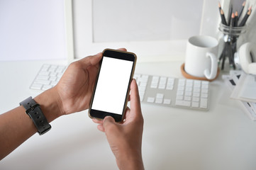 Mockup smartphone on man hands empty display with office desk background.