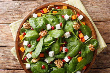 Vegetarian salad of pumpkin, spinach, goat cheese, nuts and pomegranate closeup on a plate. horizontal top view